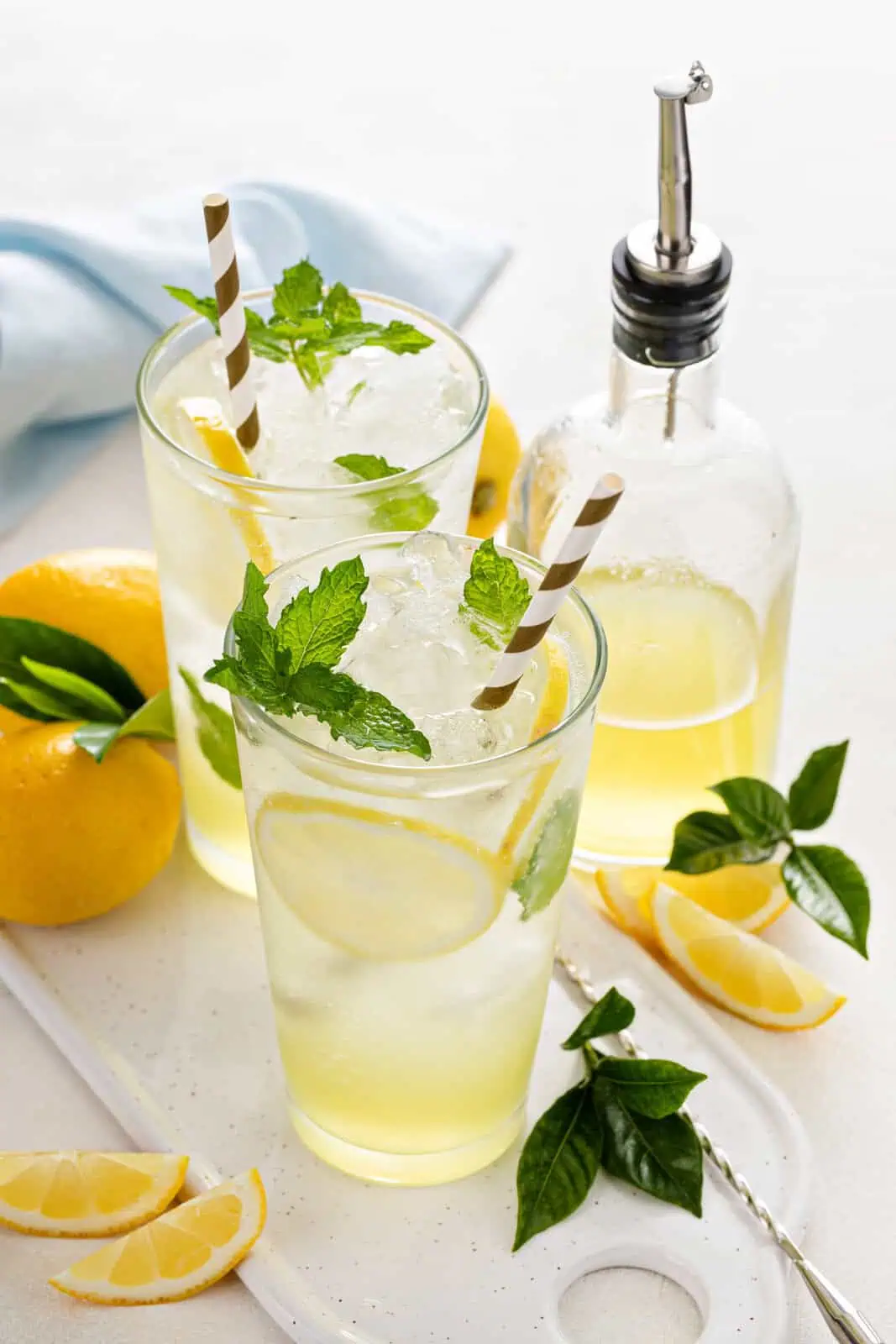 Two glasses of lemonade with a bottle of lemon syrup.