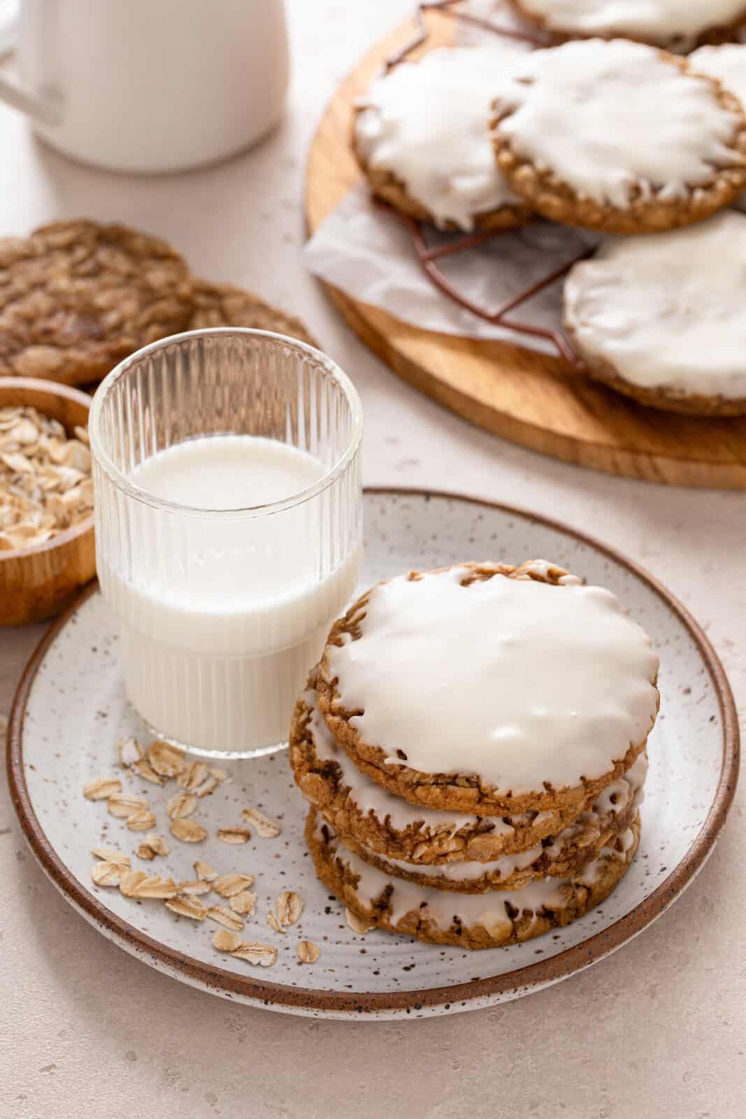 Glass of milk and a stack of iced oatmeal cookies on a plate.