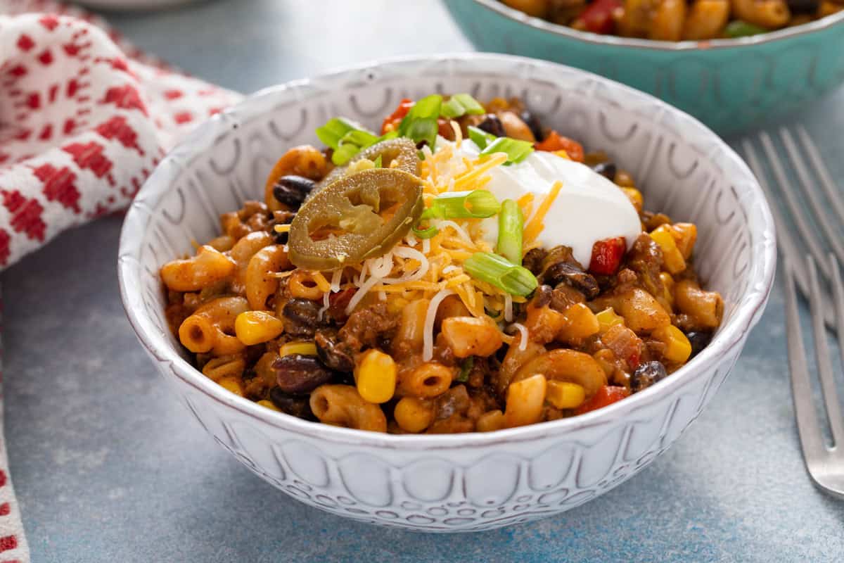 Serving of enchilada pasta in a bowl, garnished with cheese, sour cream, and pickled jalapeños.