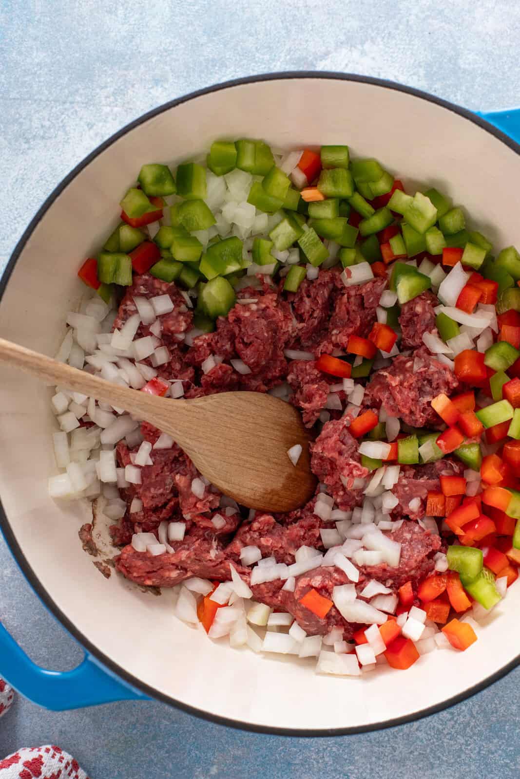 Ground beef, diced onion, and diced bell peppers added to a blue dutch oven.