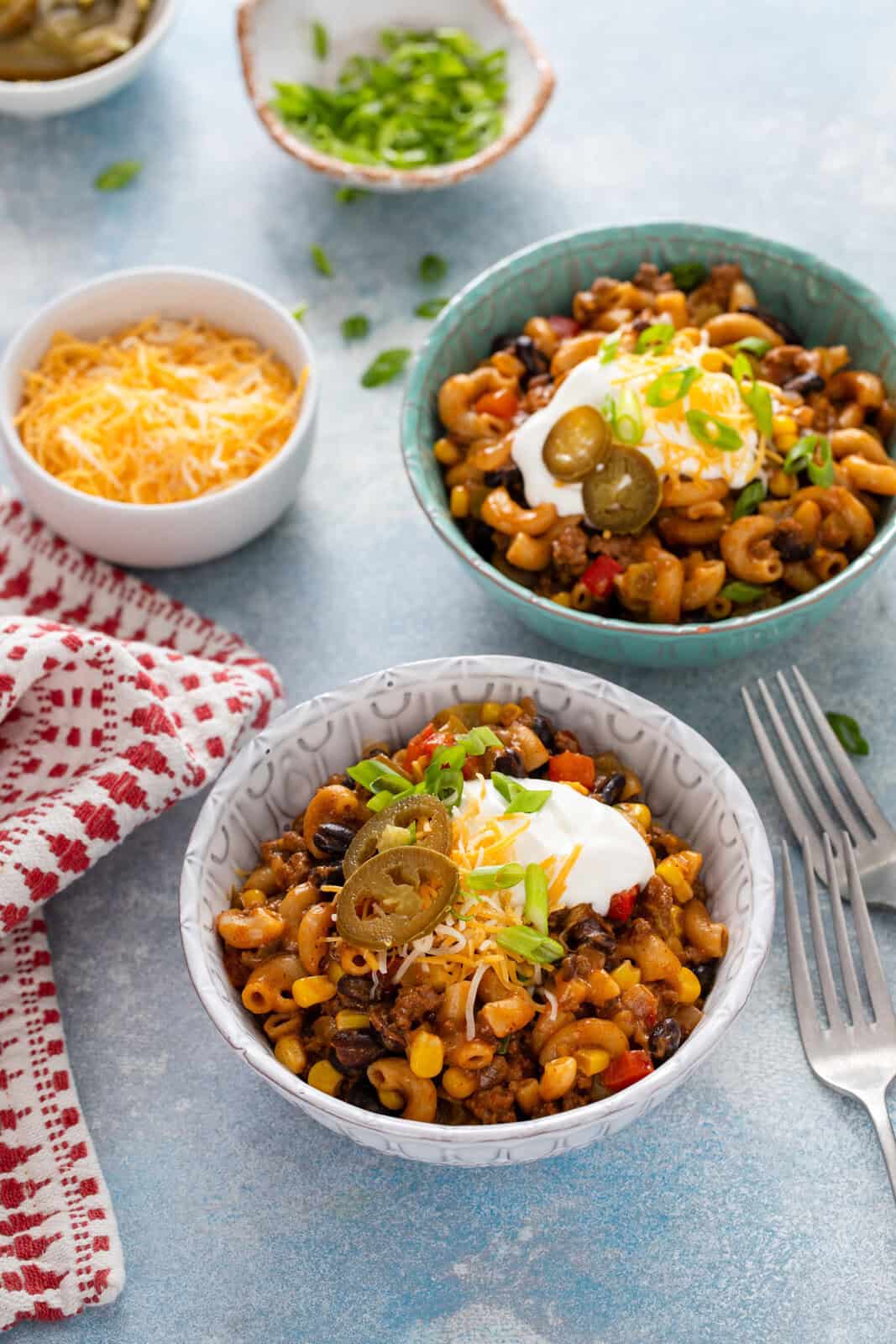 Two bowls, each holding servings of enchilada pasta topped with sour cream, cheese, and pickled jalapeños.