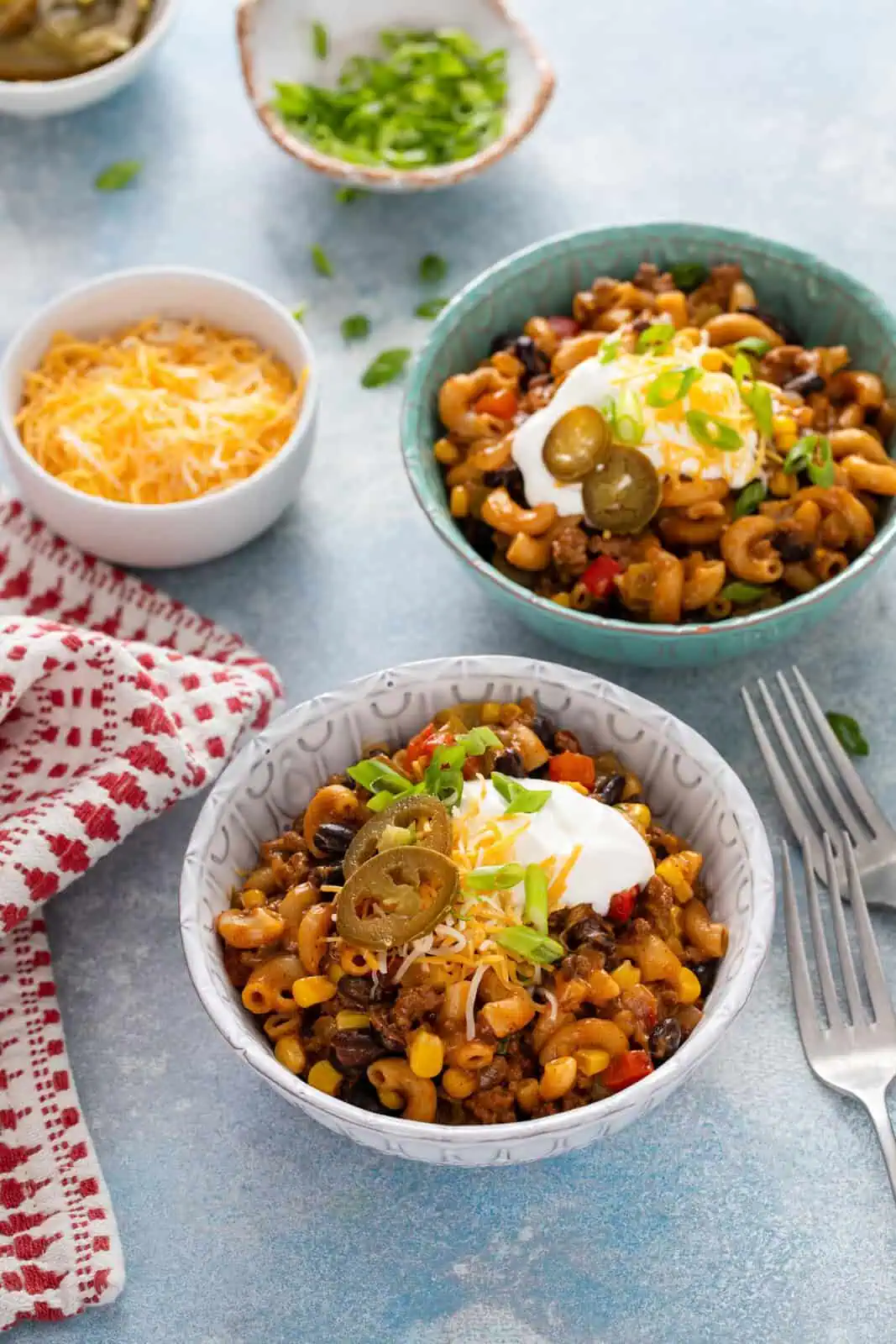 Two bowls, each holding servings of enchilada pasta topped with sour cream, cheese, and pickled jalapeños.