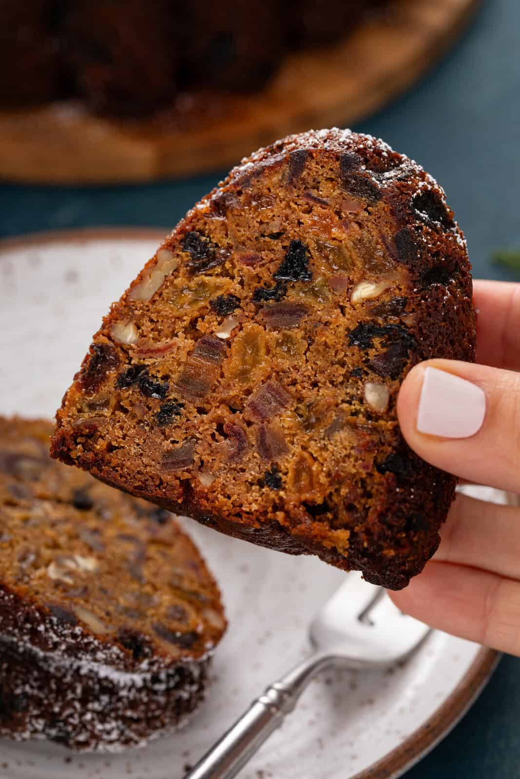 Hand holding up a slice of old-fashioned fruitcake.