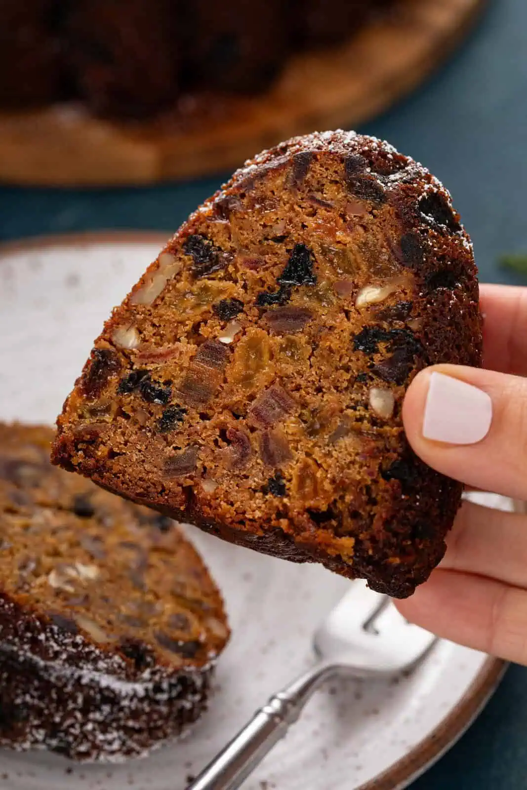 Hand holding up a slice of old-fashioned fruitcake.
