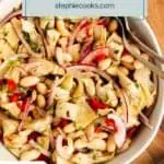 Overhead view of a white bowl on a countertop, filled with white bean and artichoke salad. Text overlay includes recipe name.