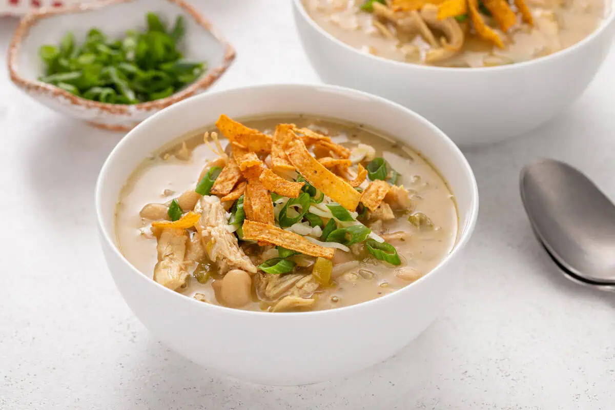 White bean chicken chili in a white bowl, garnished with green onions and tortilla strips.