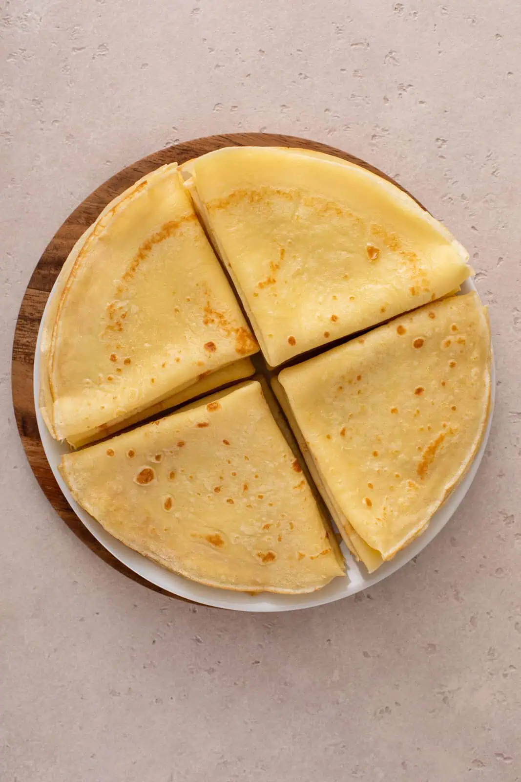 Cooked crepes folded and stacked on a large white plate.