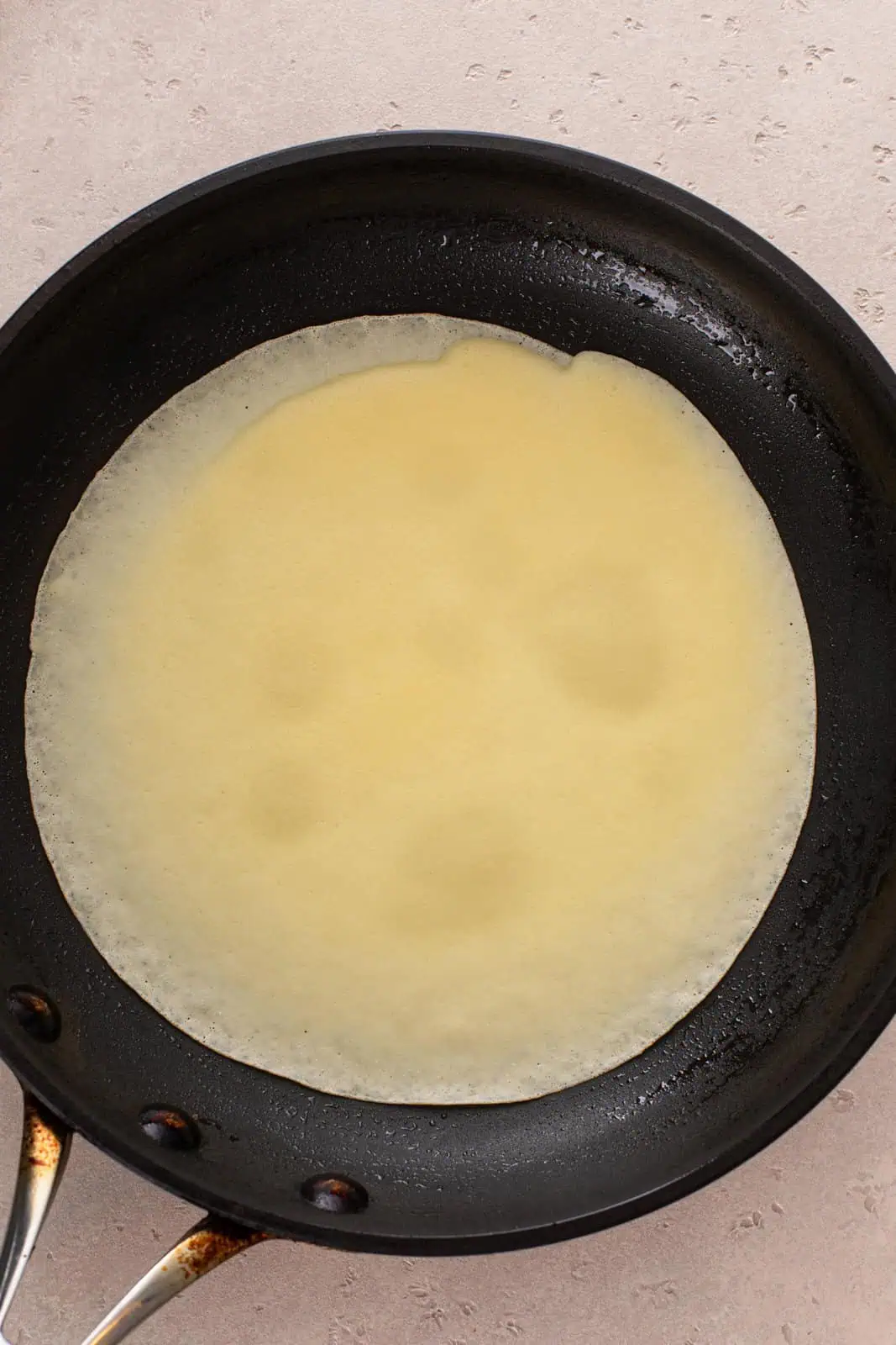 Crepe cooking in a pan, ready to be flipped.