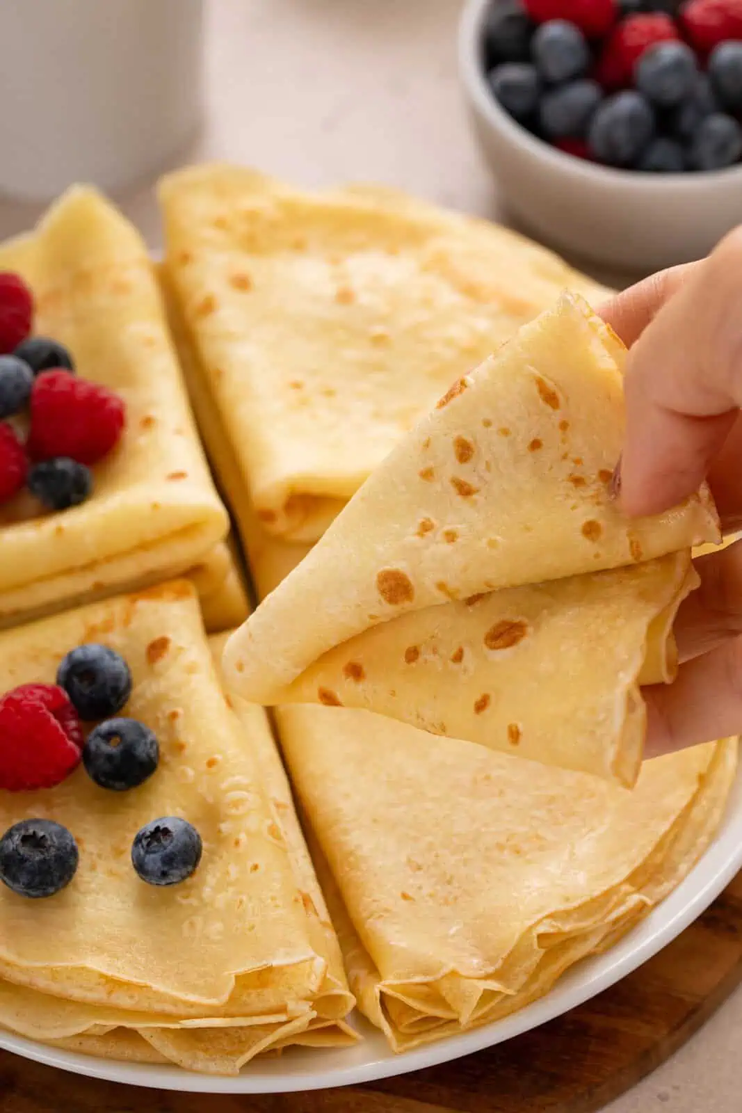 Person picking up a plate from a platter of folded crepes.