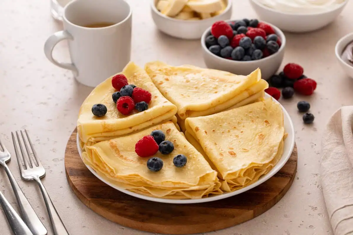 Crepes folded and stacked on a white plate and garnished with fresh berries.