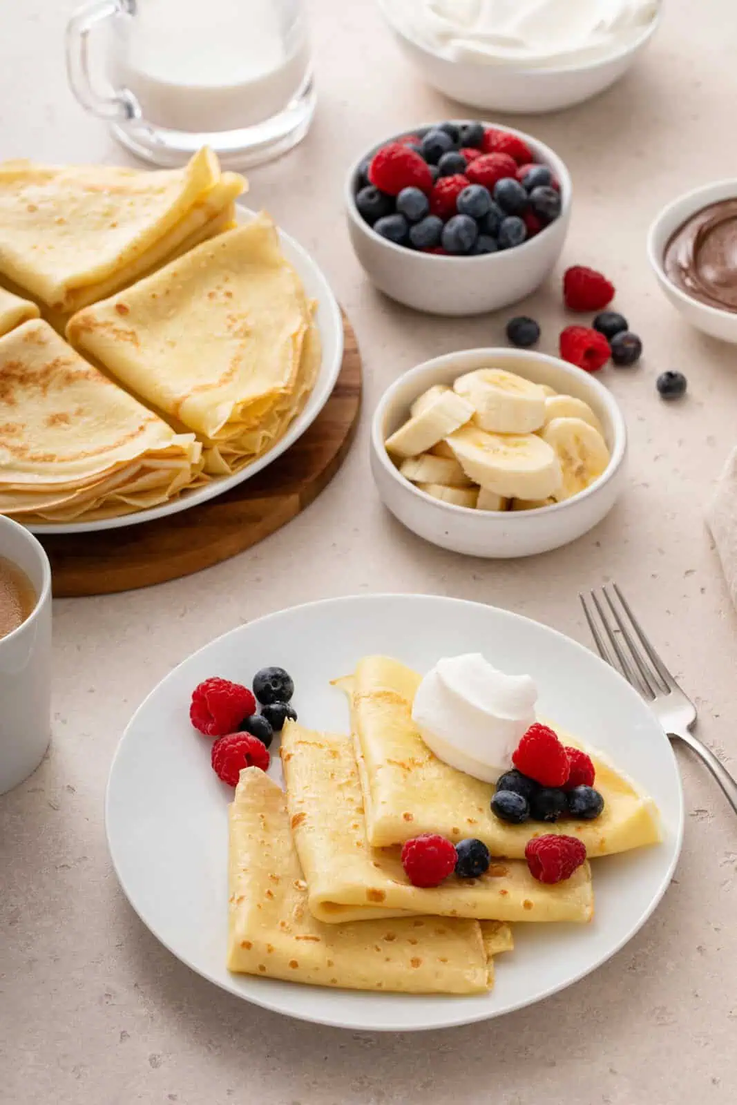 White plate holding 3 folded crepes topped with berries and whipped cream.