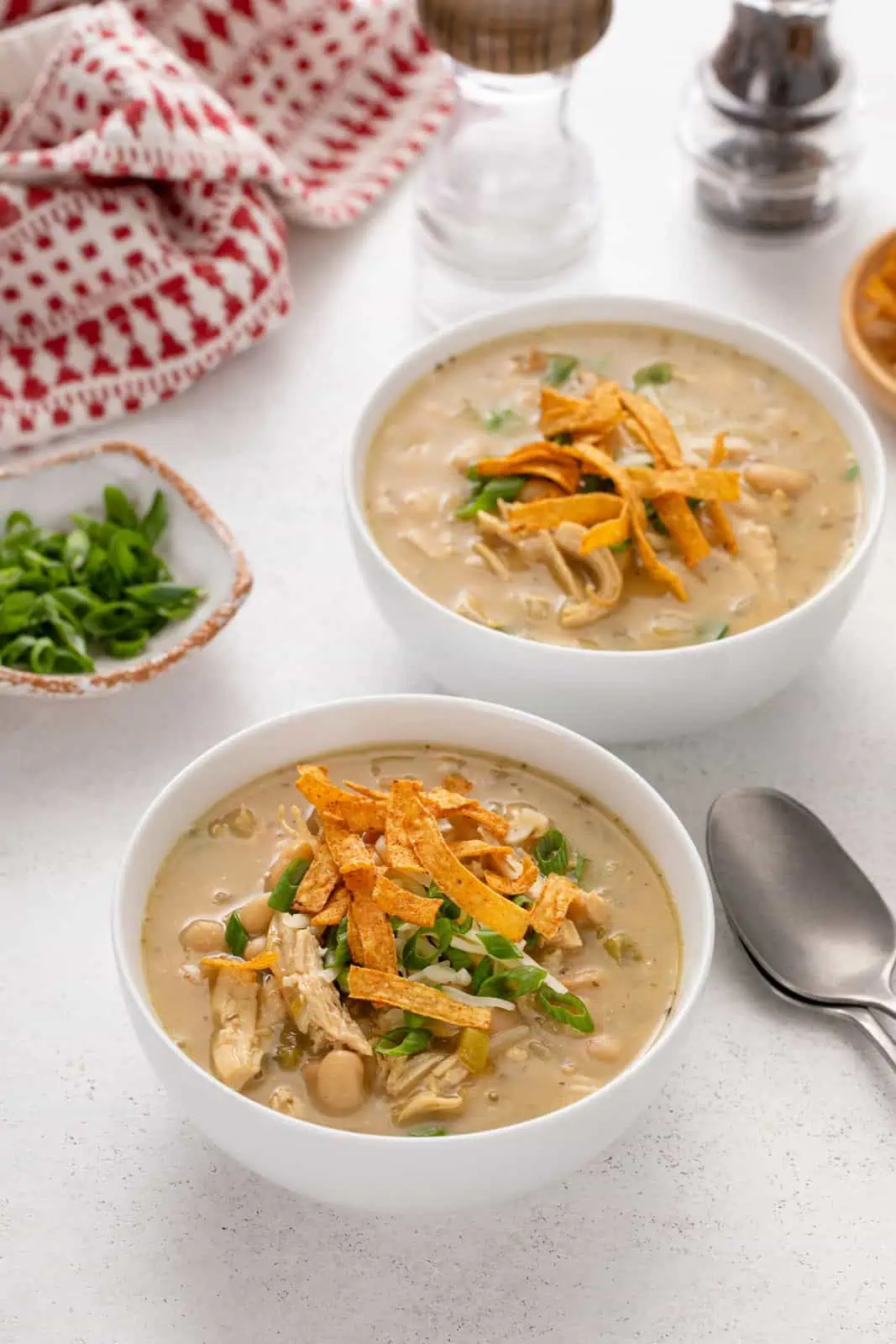 Two white bowls filled with white bean chicken chili and garnished with green onions and tortilla strips.