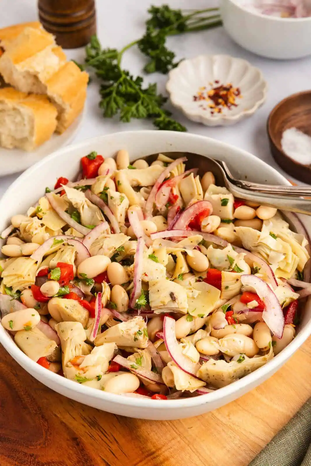 White serving bowl filled with white bean and artichoke salad.