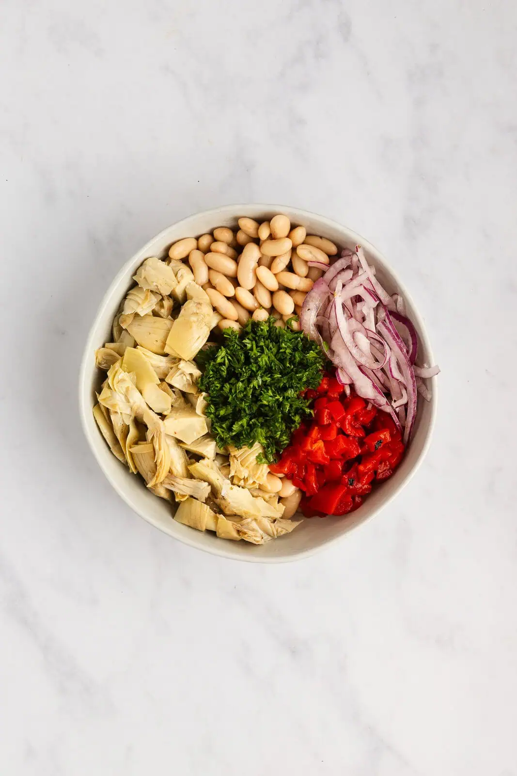 Ingredients for white bean salad added to a mixing bowl.