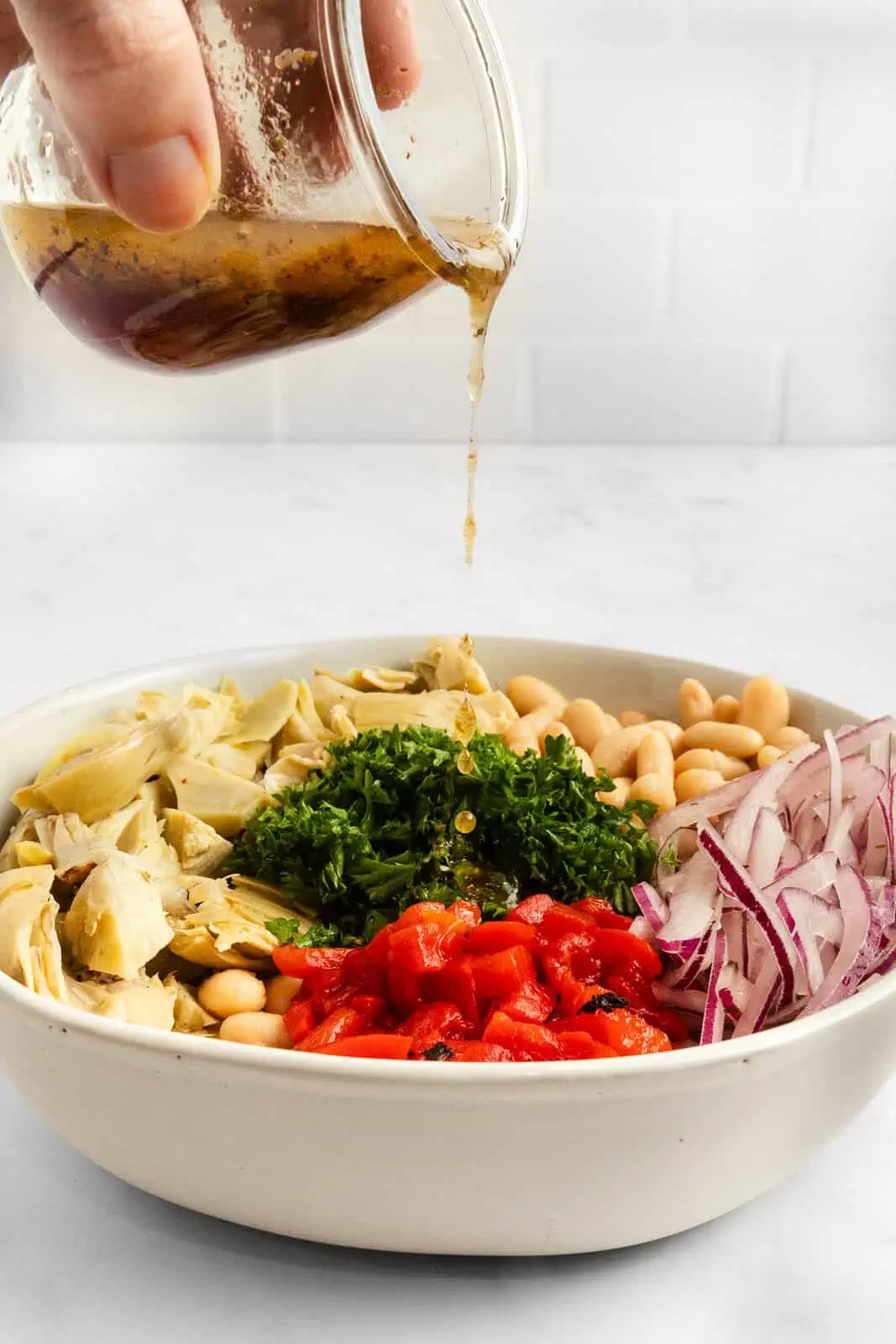 Dressing being poured over white bean salad in a white bowl.