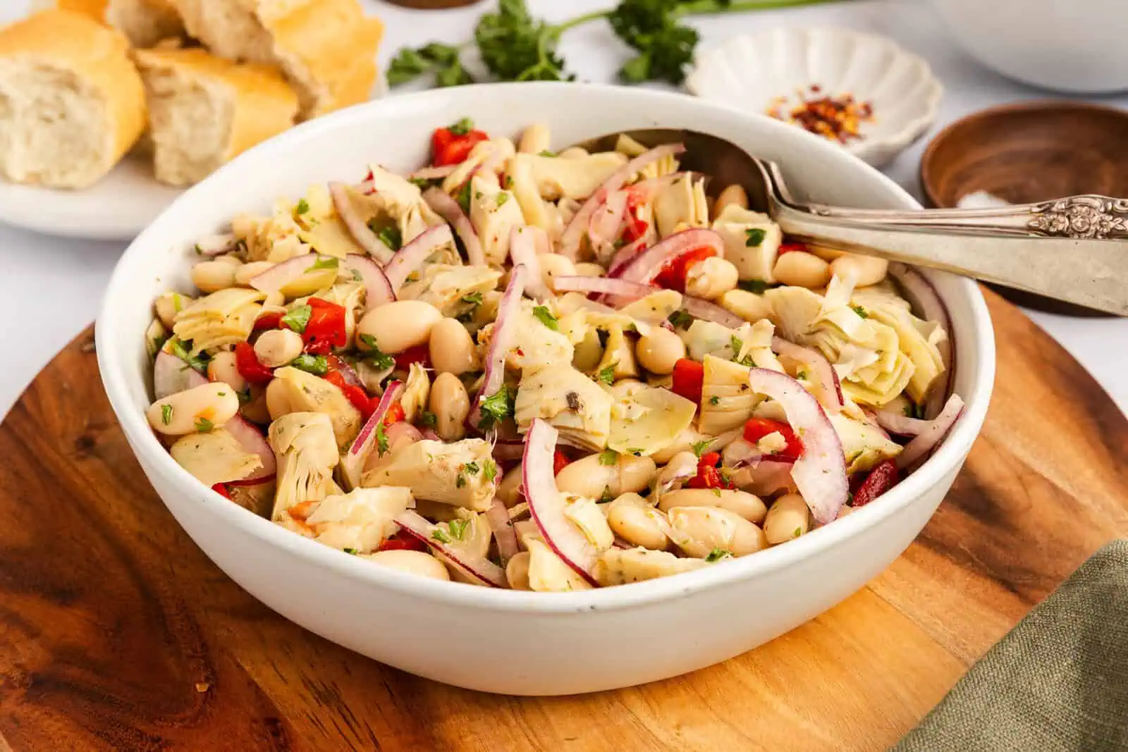 White serving bowl on a wooden board, filled with white bean and artichoke salad.