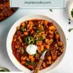 Spoon in a bowl of turkey sweet potato chili garnished with a dollop of sour cream. Text overlay includes recipe name.