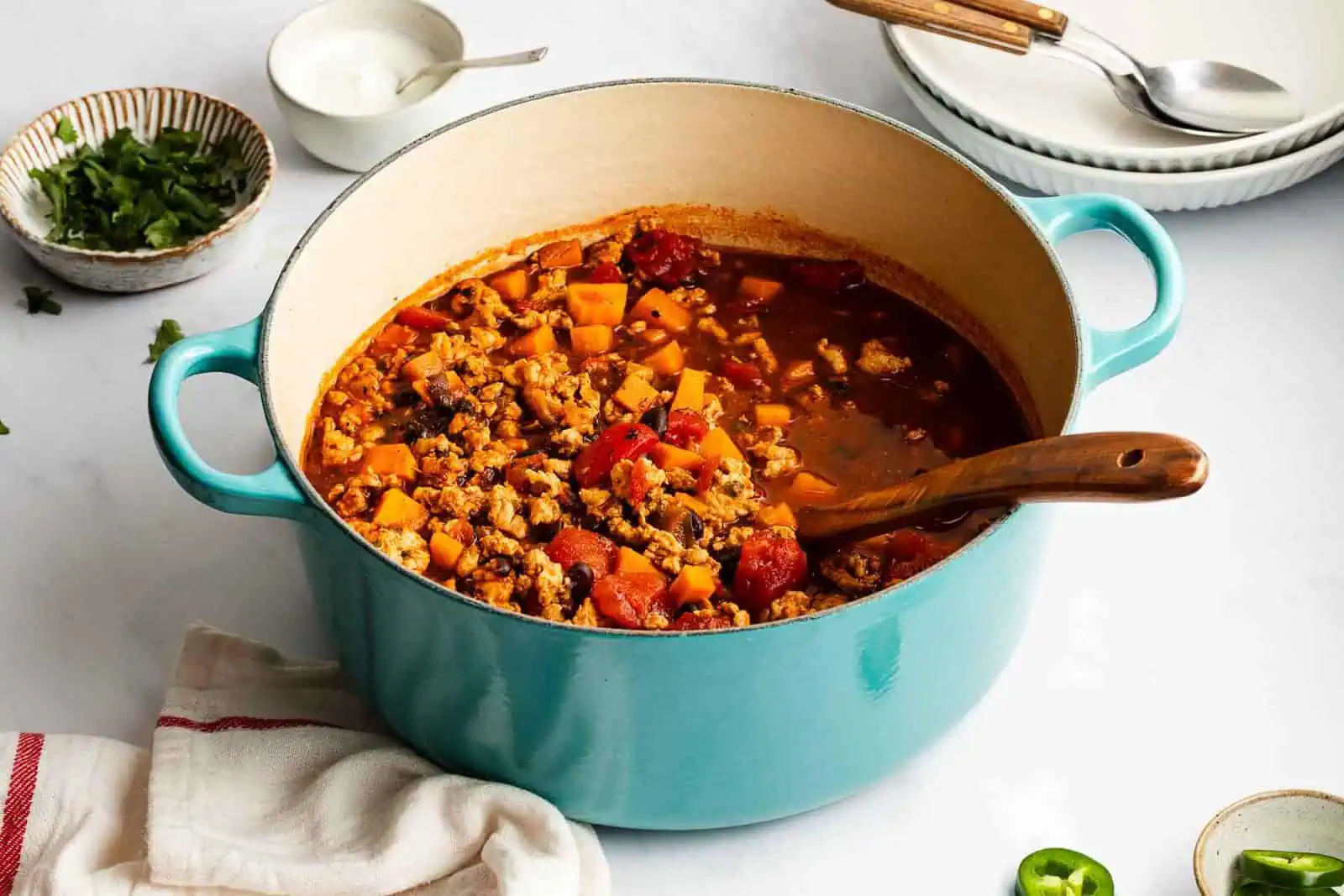 Wooden spoon in a blue pot filled with turkey sweet potato chili.