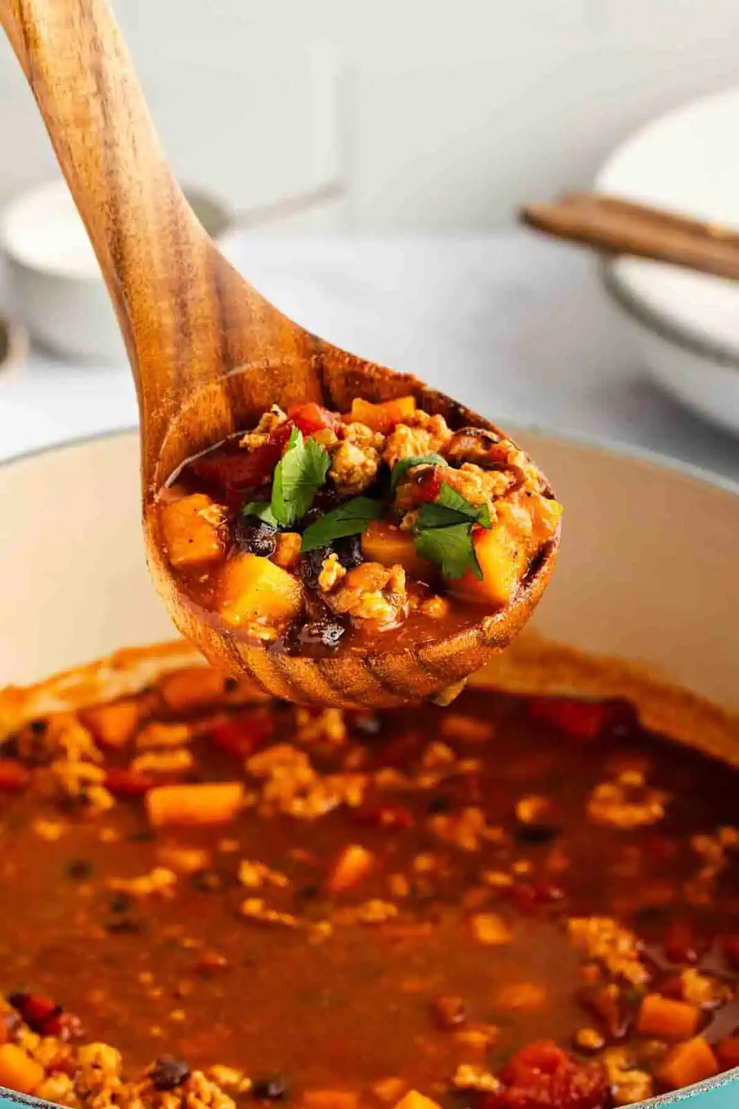 Wooden ladle lifting up a serving of turkey sweet potato chili.