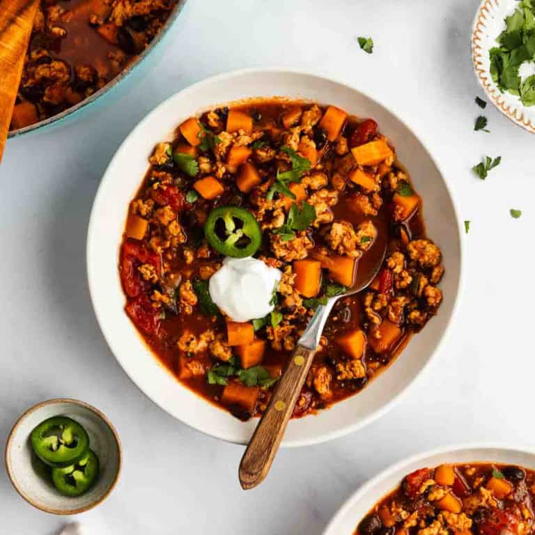 Spoon in a bowl of turkey sweet potato chili garnished with a dollop of sour cream.
