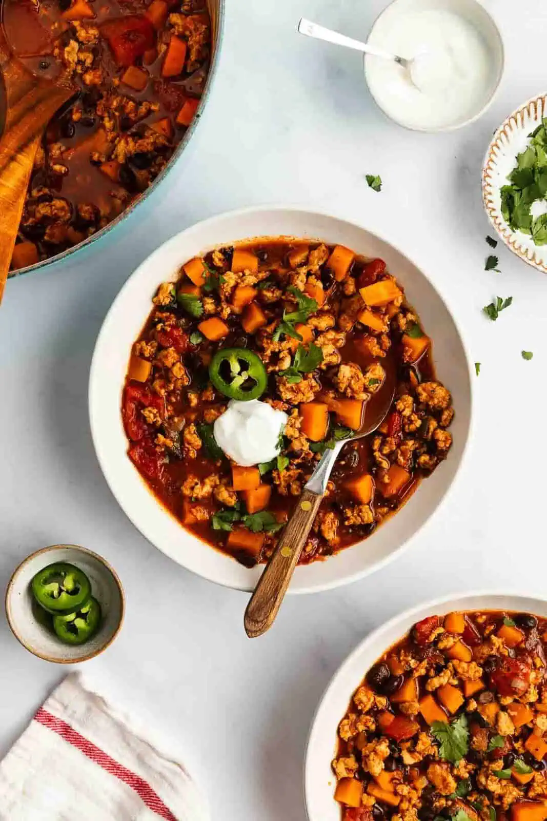 Overhead view of a white bowl filled with sweet potato chili on a countertop between a second bowl of chili and the pot of chili.