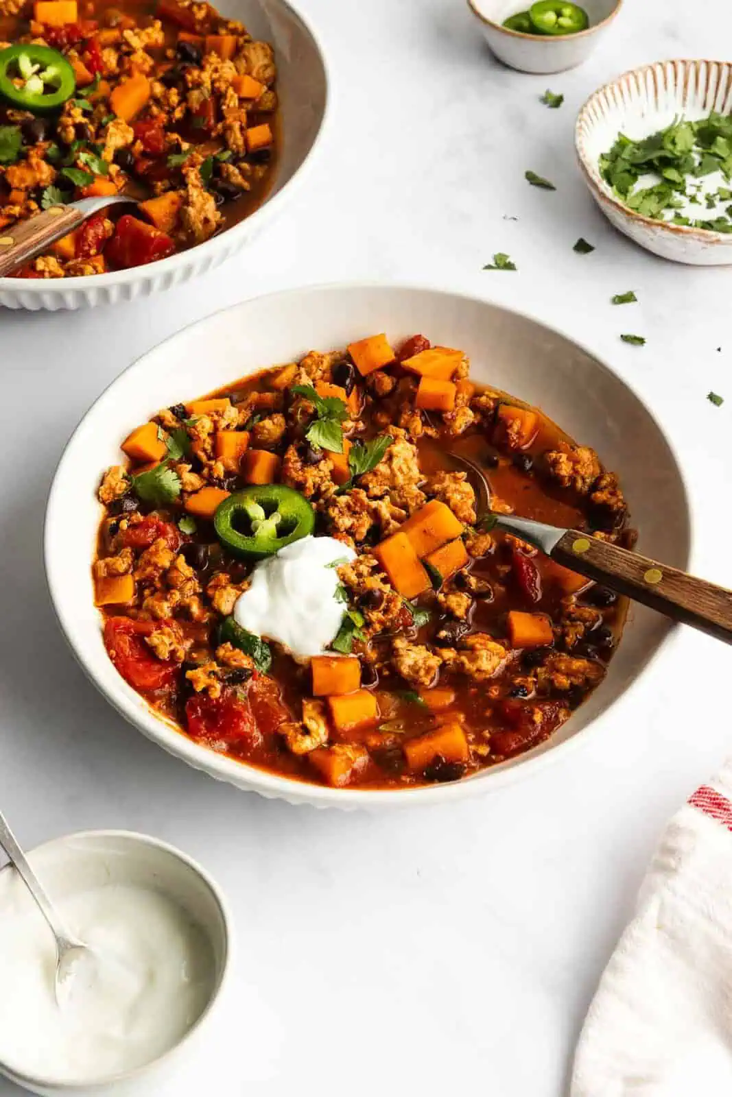 White bowl filled with turkey sweet potato chili, garnished with a dollop of sour cream.