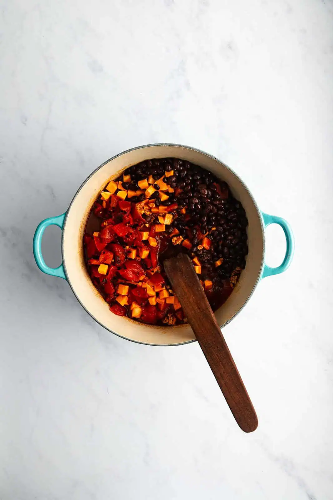 Black beans, sweet potatoes, and tomatoes added to a pot for sweet potato chili.