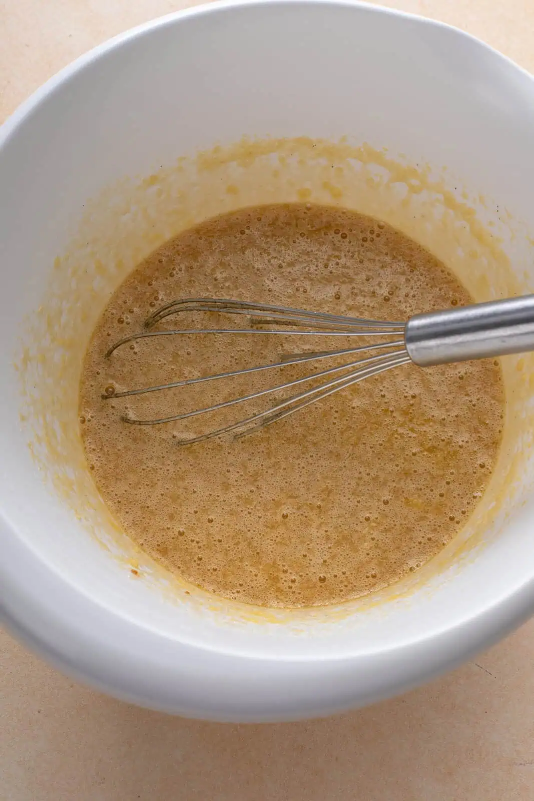 Eggs, sugar, butter, vanilla, and syrup whisked together in a white mixing bowl.