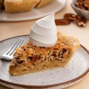 Slice of oatmeal pie next to a fork on a plate. the pie is topped with a dollop of whipped cream.