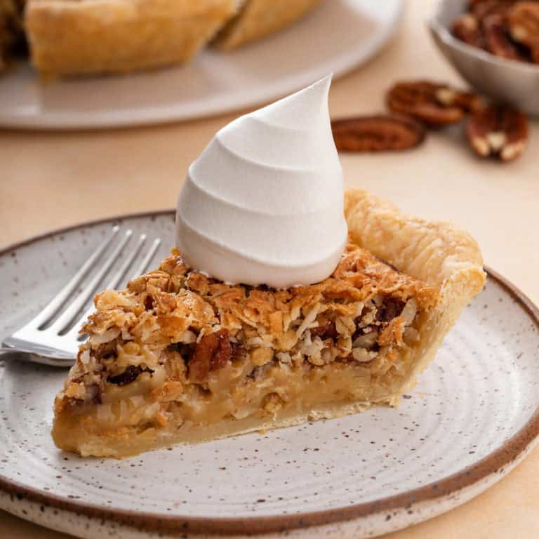 Slice of oatmeal pie next to a fork on a plate. the pie is topped with a dollop of whipped cream.