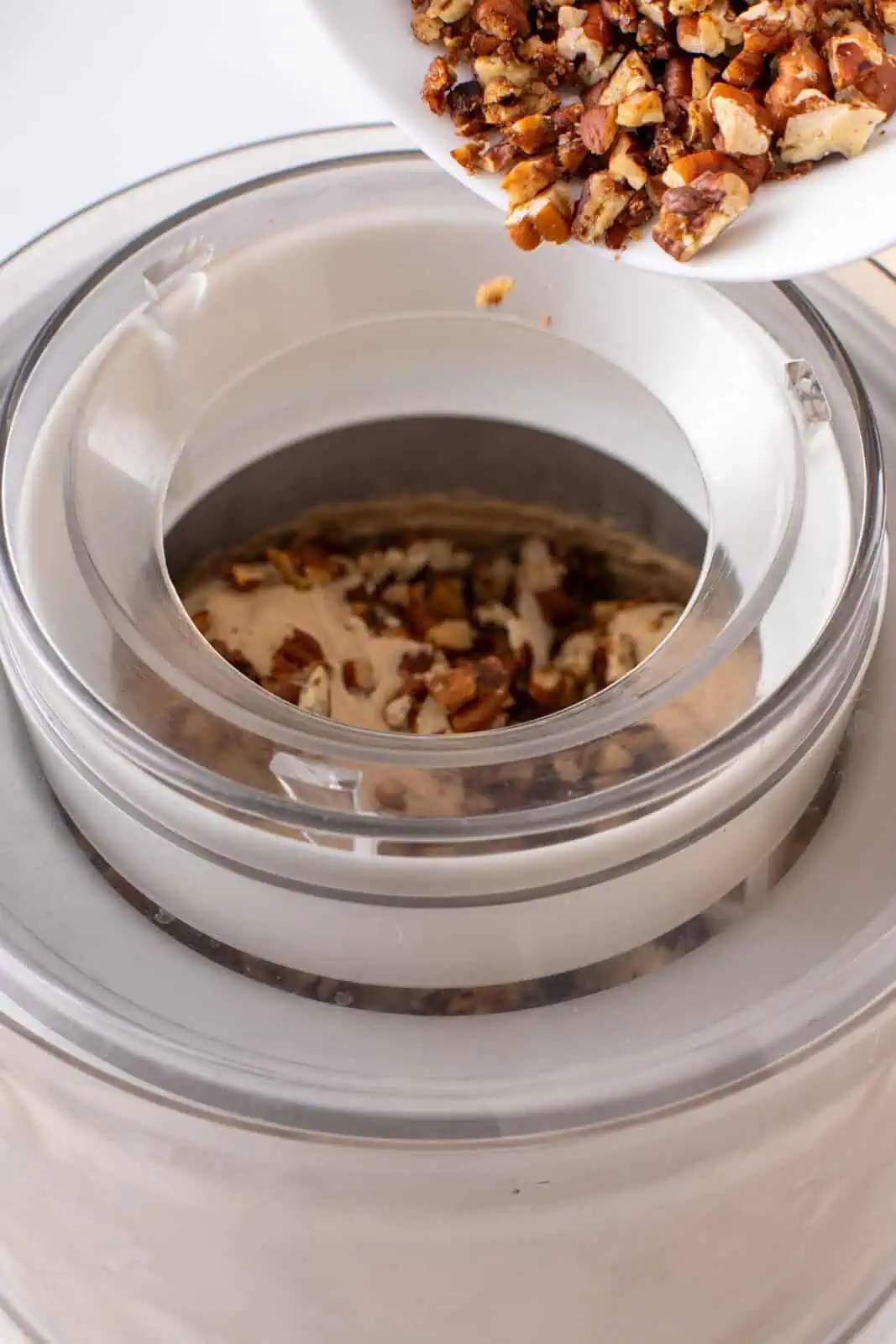 Toasted pecans being added to an ice cream maker with churned base.