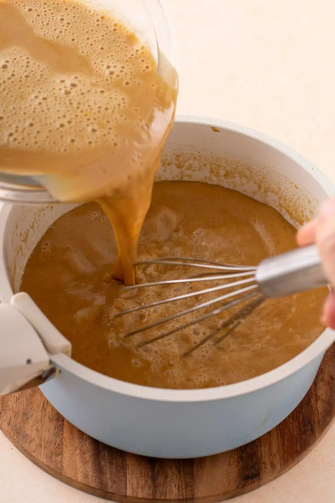 Hot egg yolk mixture being added back into a saucepan.