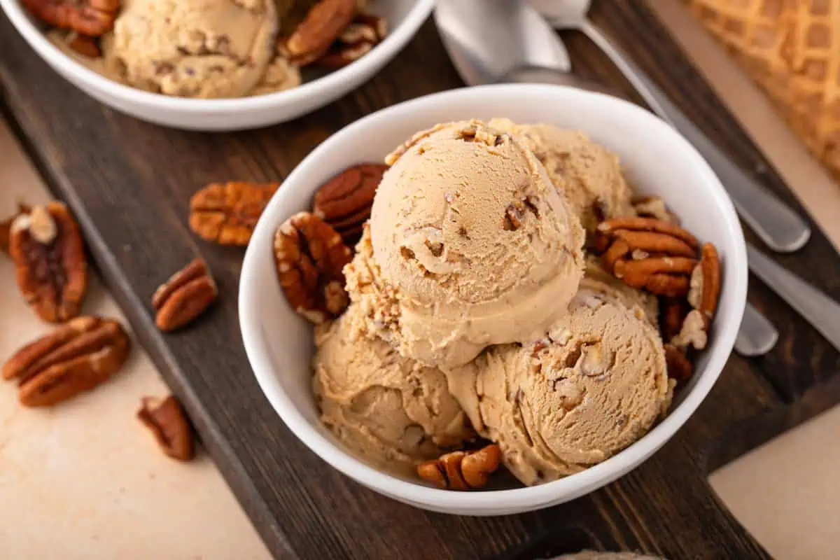 White bowl filled with several scoops of butter pecan ice cream and pecan halves.