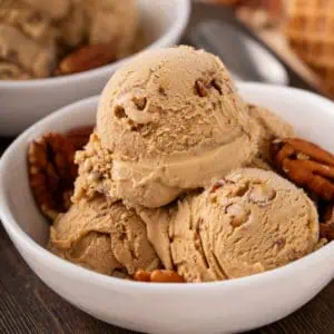 Scoops of butter pecan ice cream and pecan halves in a white bowl.