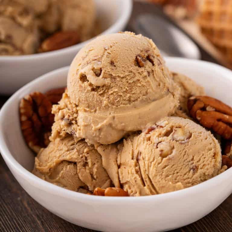 Scoops of butter pecan ice cream and pecan halves in a white bowl.