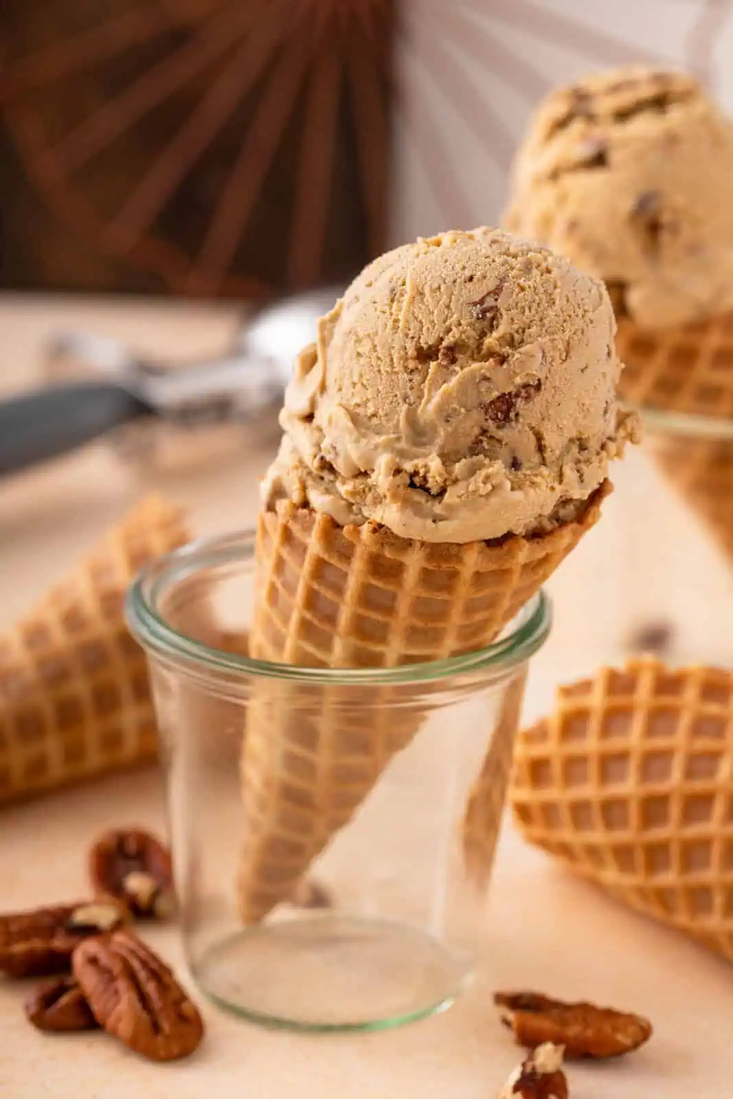 Waffle cone with a scoop of butter pecan ice cream set up in a glass cup.