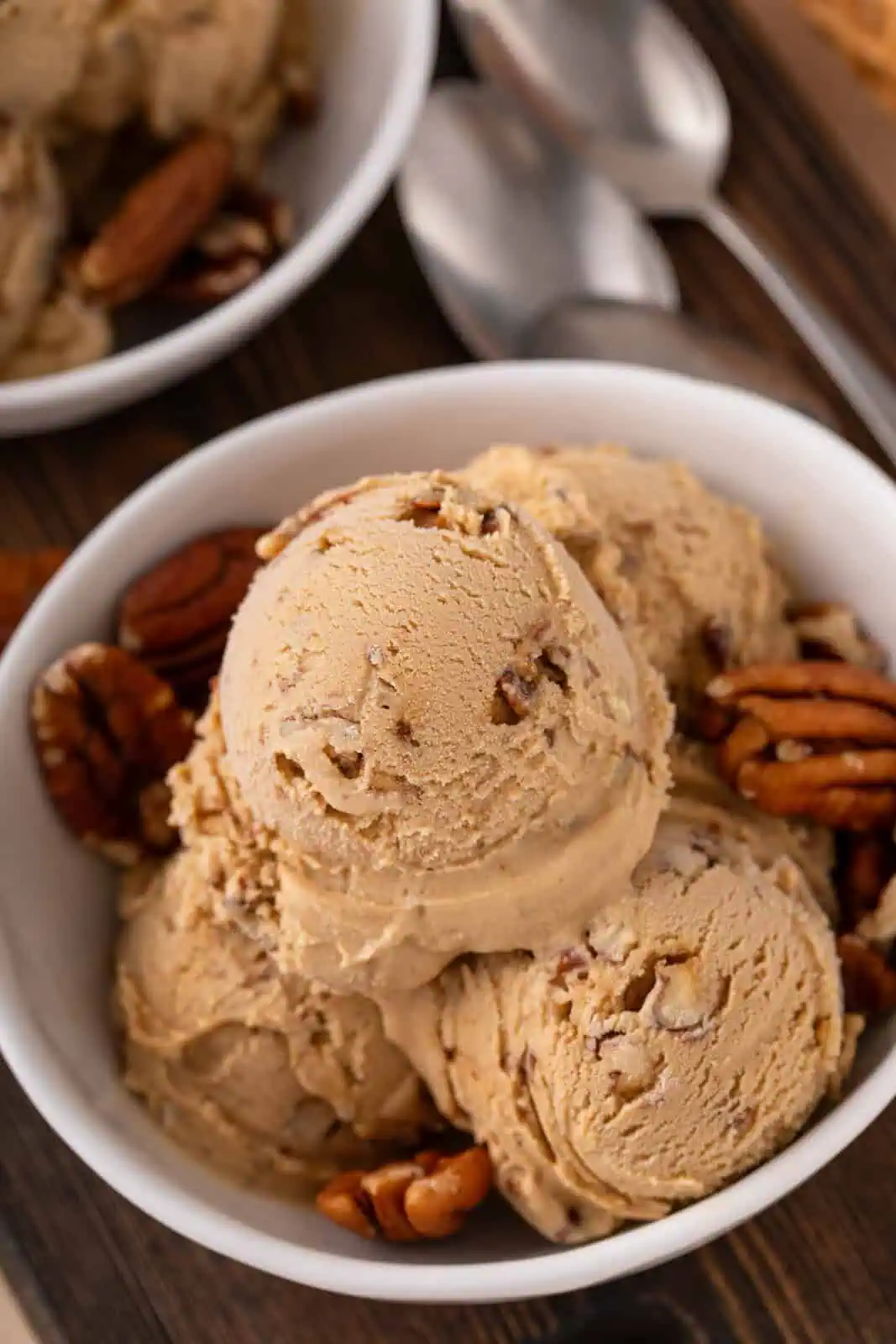 Close up of scoops of butter pecan ice cream and pecan halves in a white bowl.