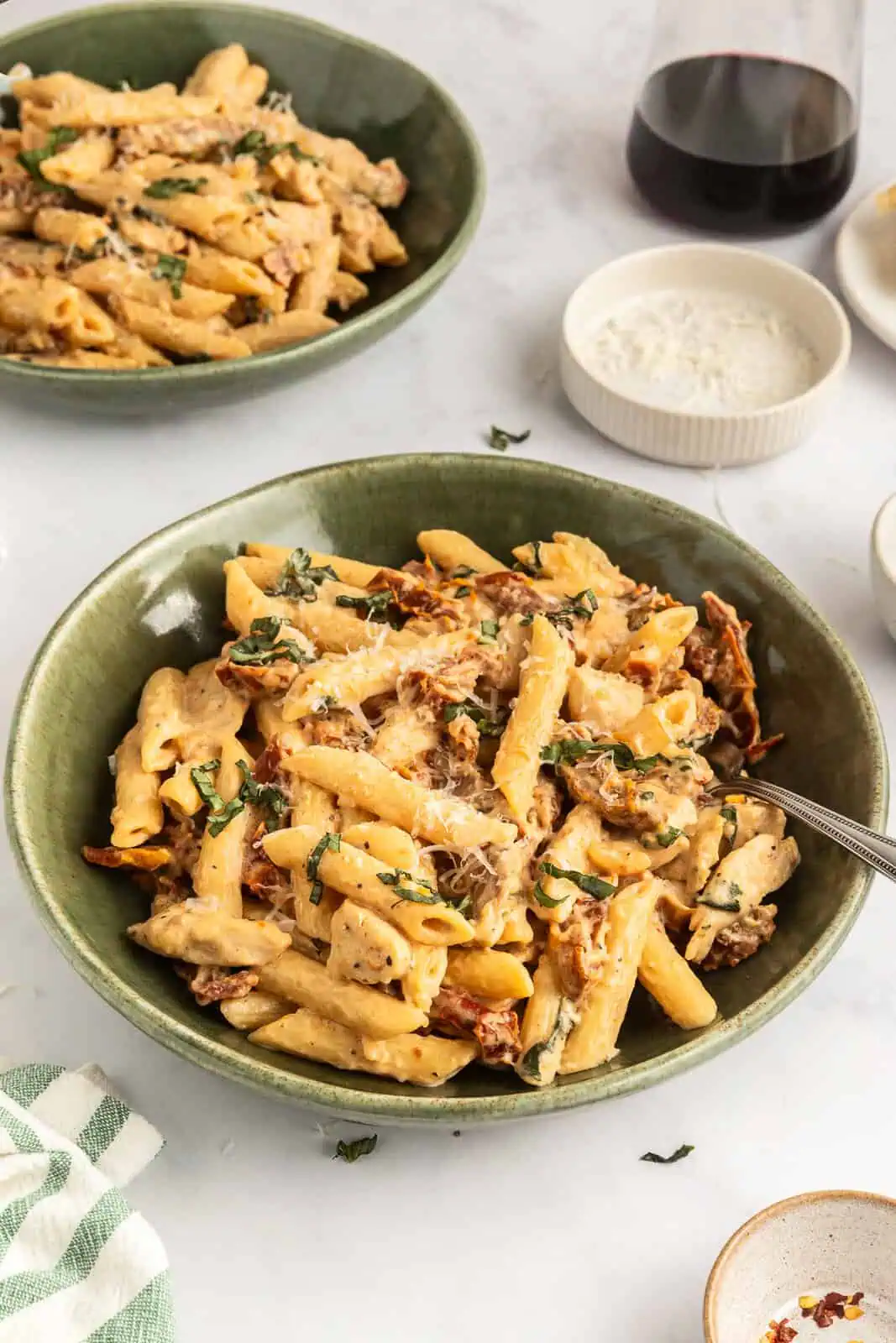 Two green pasta bowls filled with sun-dried tomato pasta arranged on a countertop.