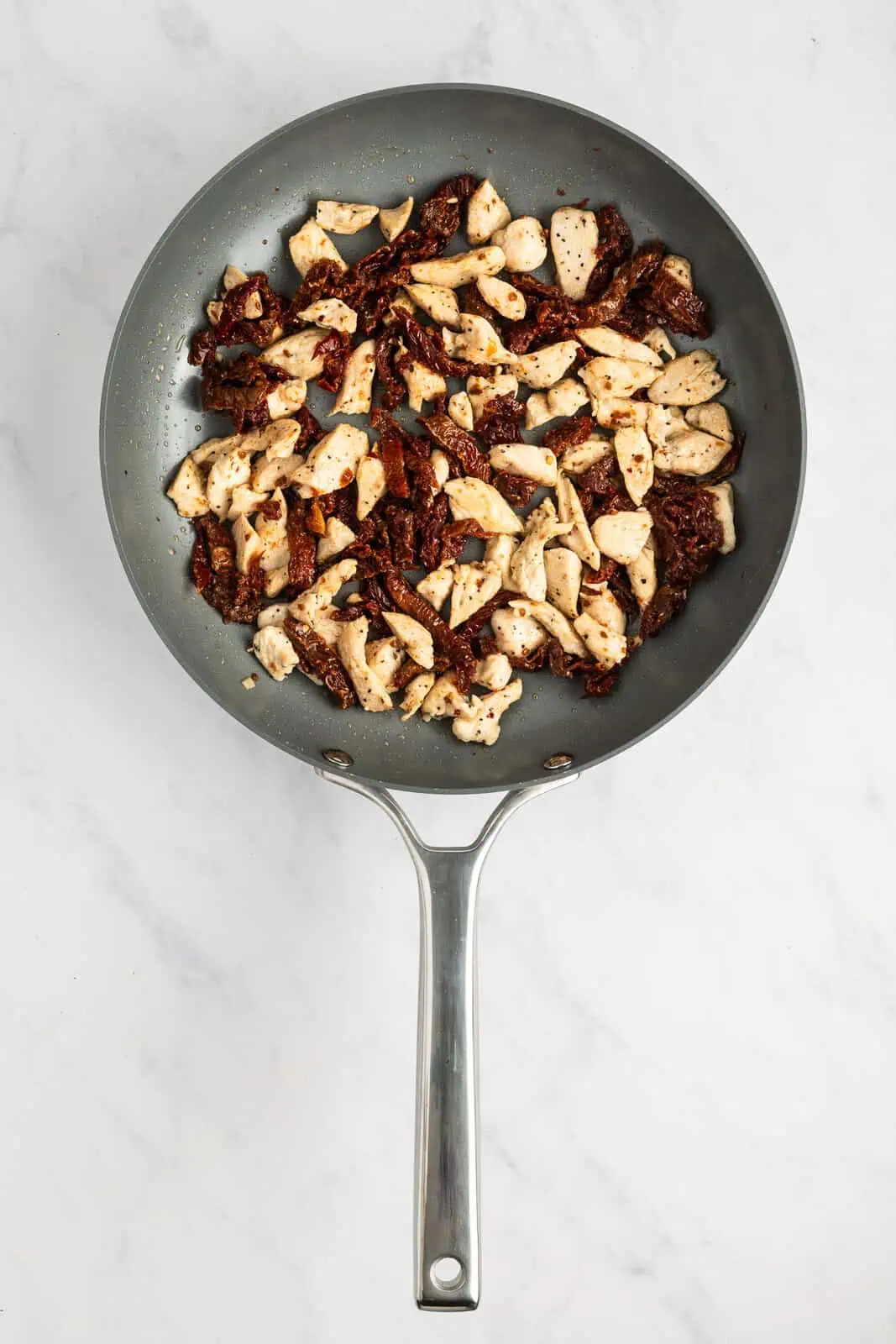 Seared chicken and sun-dried tomatoes being sautéed in a skillet.