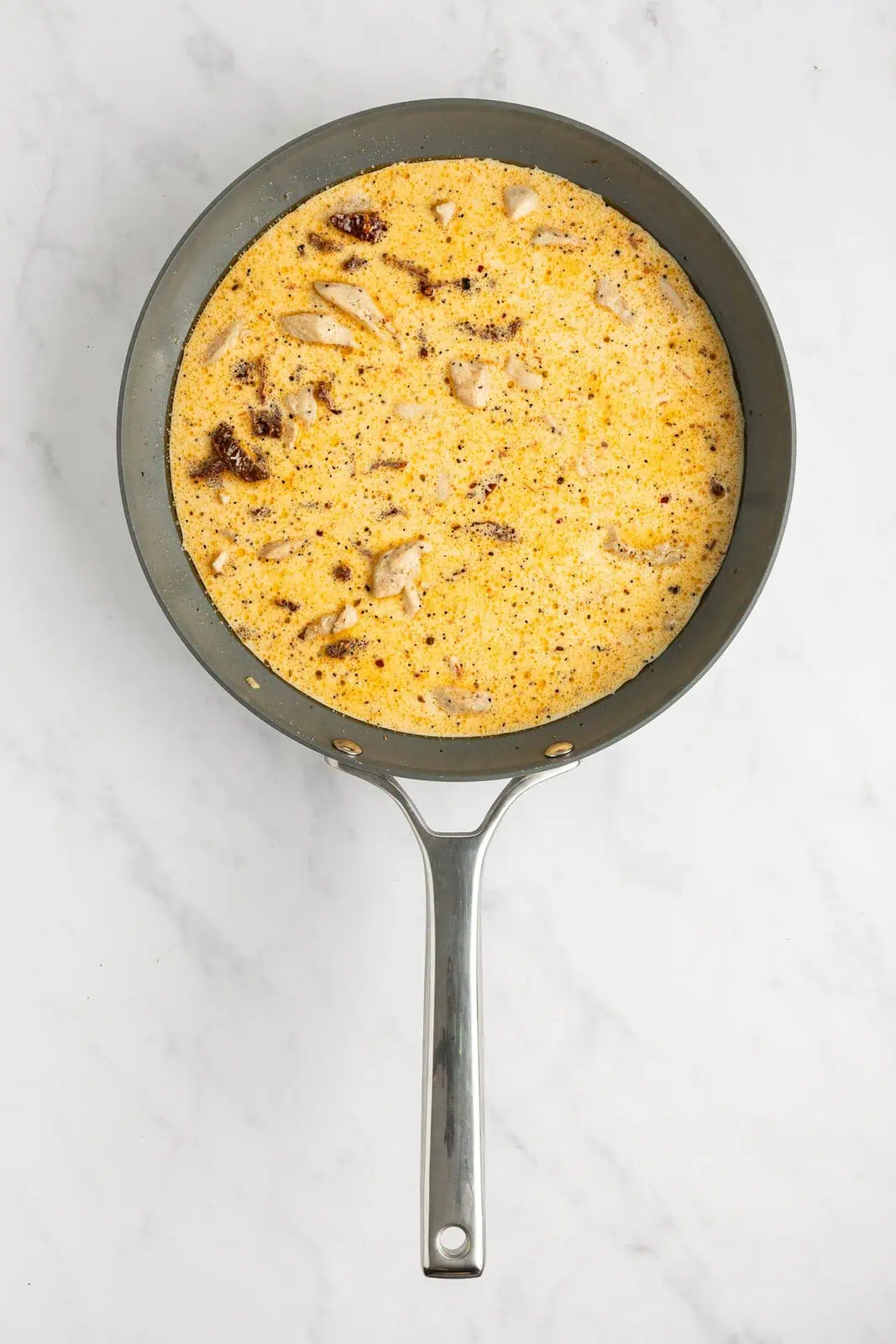 Cream sauce for sun-dried tomato pasta simmering in a skillet.