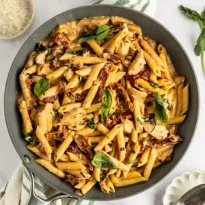 Overhead view of chicken and sun-dried tomato pasta in a skillet, garnished with fresh basil.