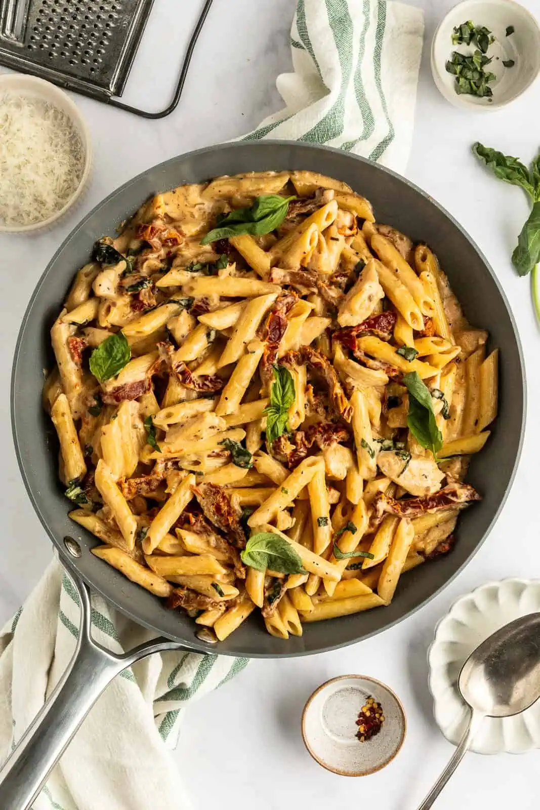 Overhead view of a skillet filled with sun-dried tomato pasta set on a countertop.