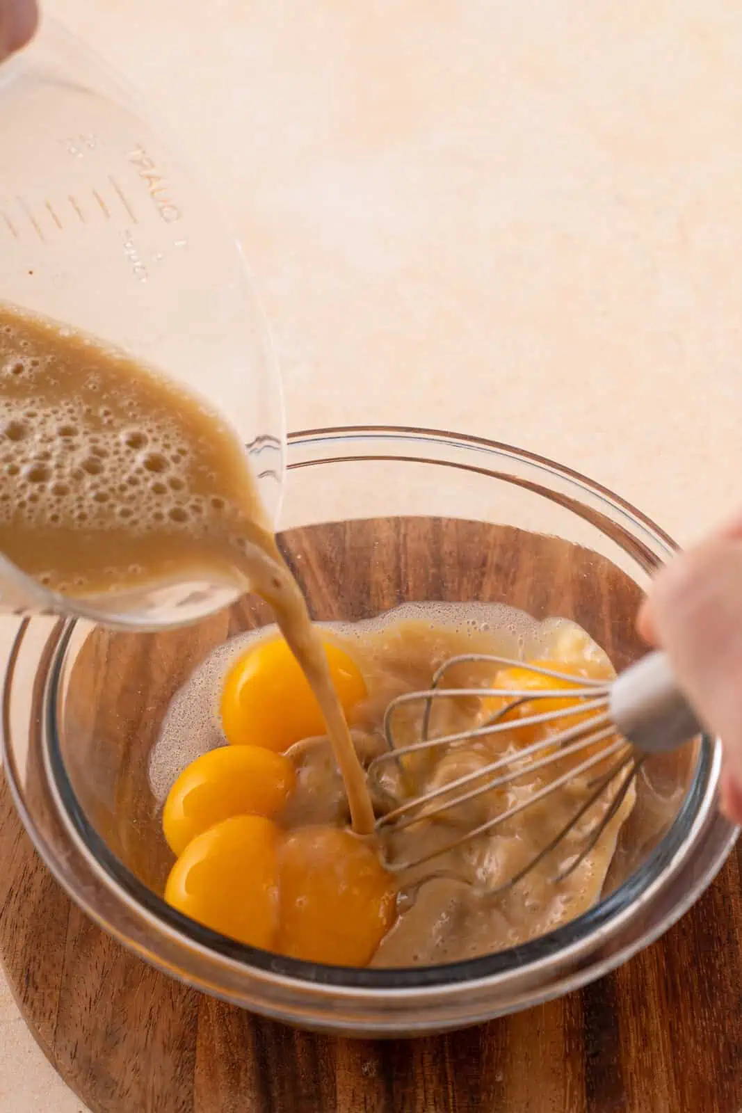 Hot ice cream base mixture being added to egg yolks in a glass bowl for tempering.