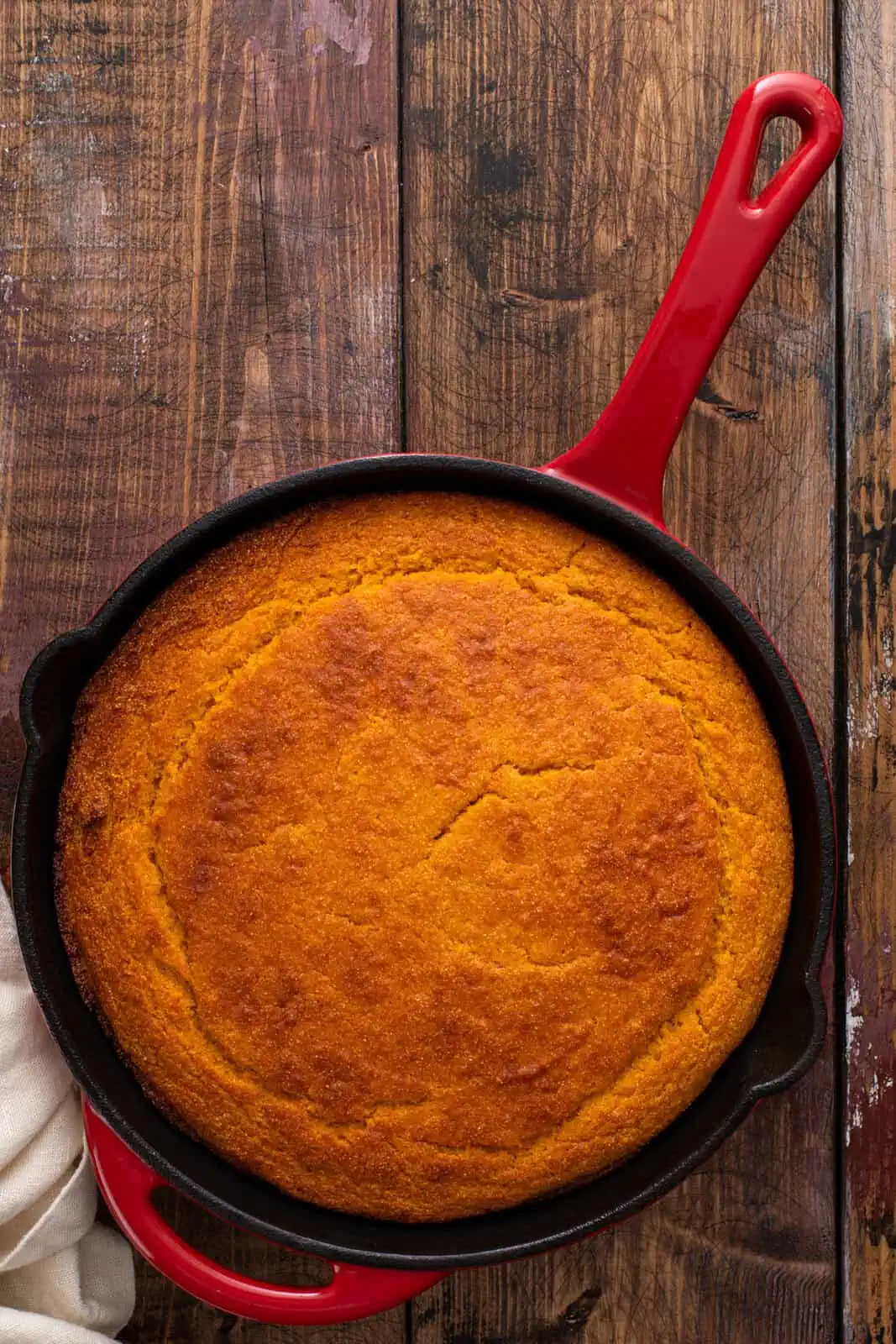 Skillet of baked sweet potato cornbread resting on a wooden table.