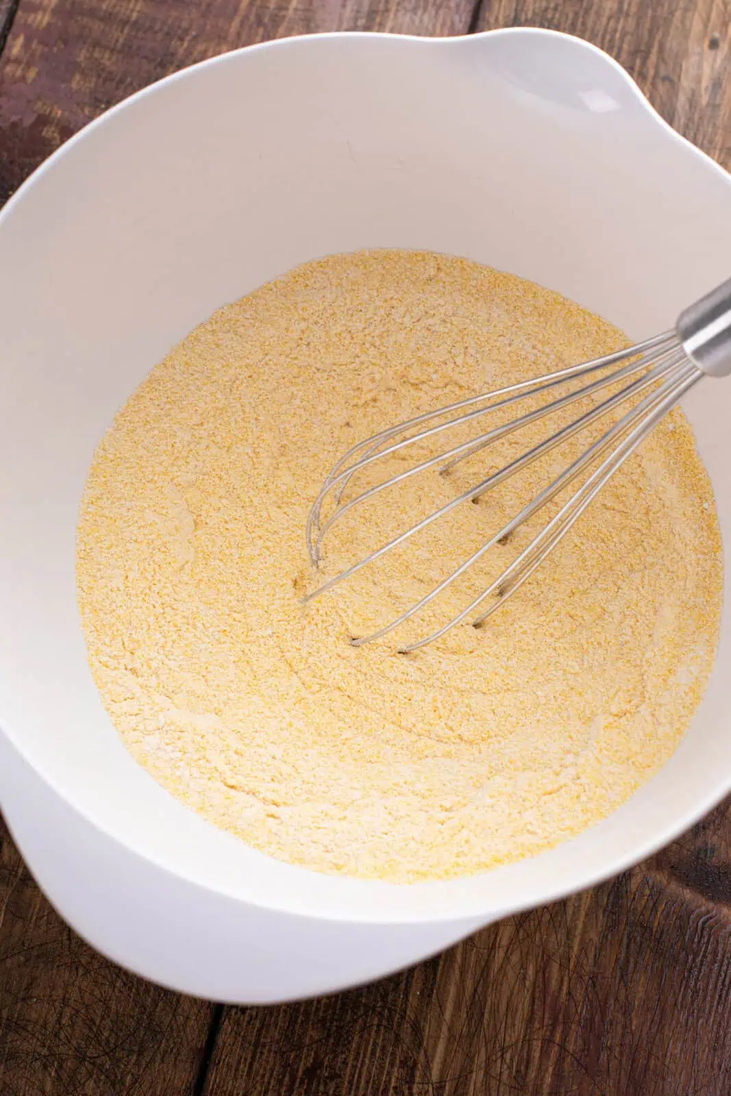 Dry ingredients for sweet potato cornbread whisked in a white bowl.