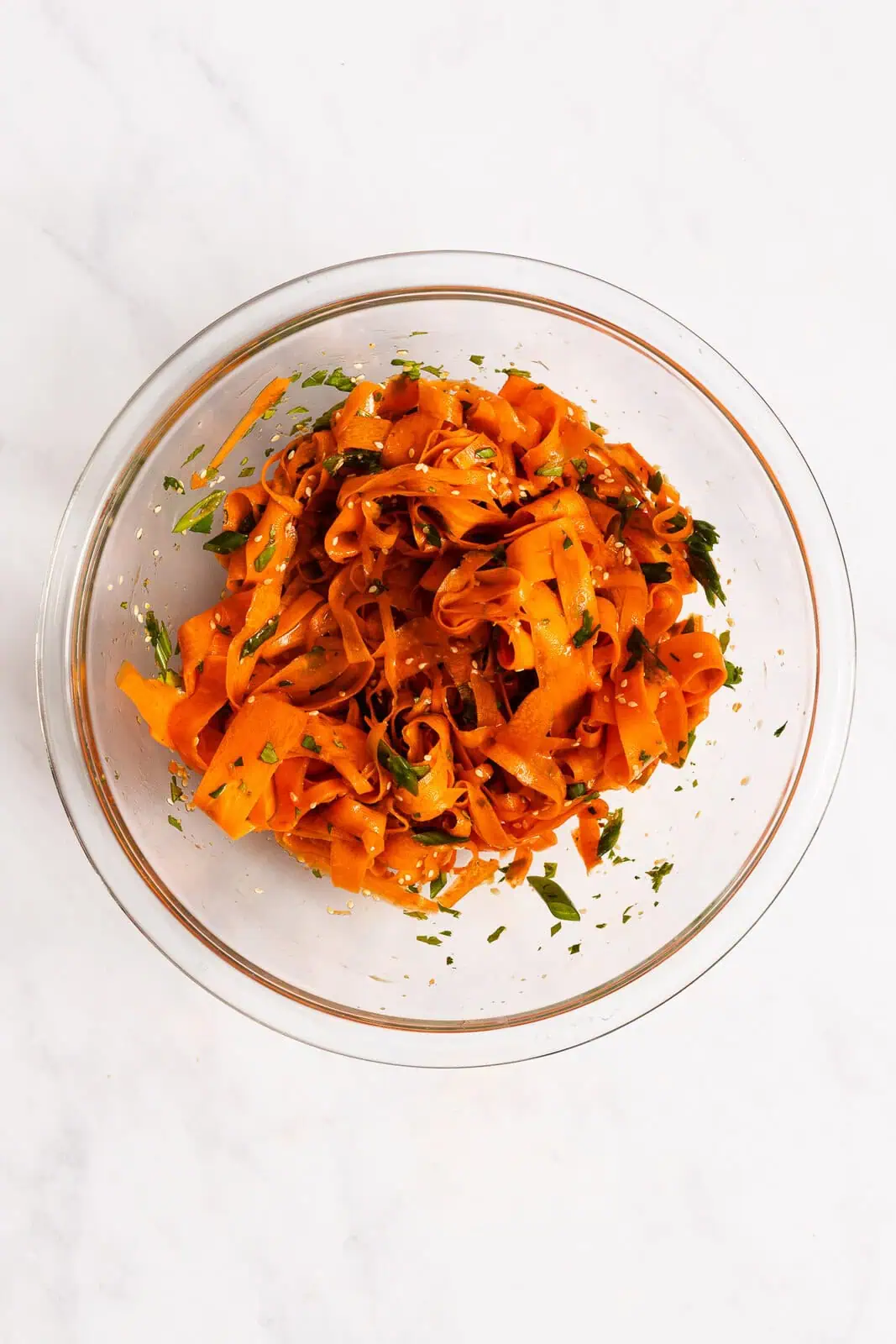 Freshly tossed shaved carrot salad in a glass mixing bowl.