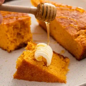 Honey being drizzled over pieces of sweet potato cornbread.