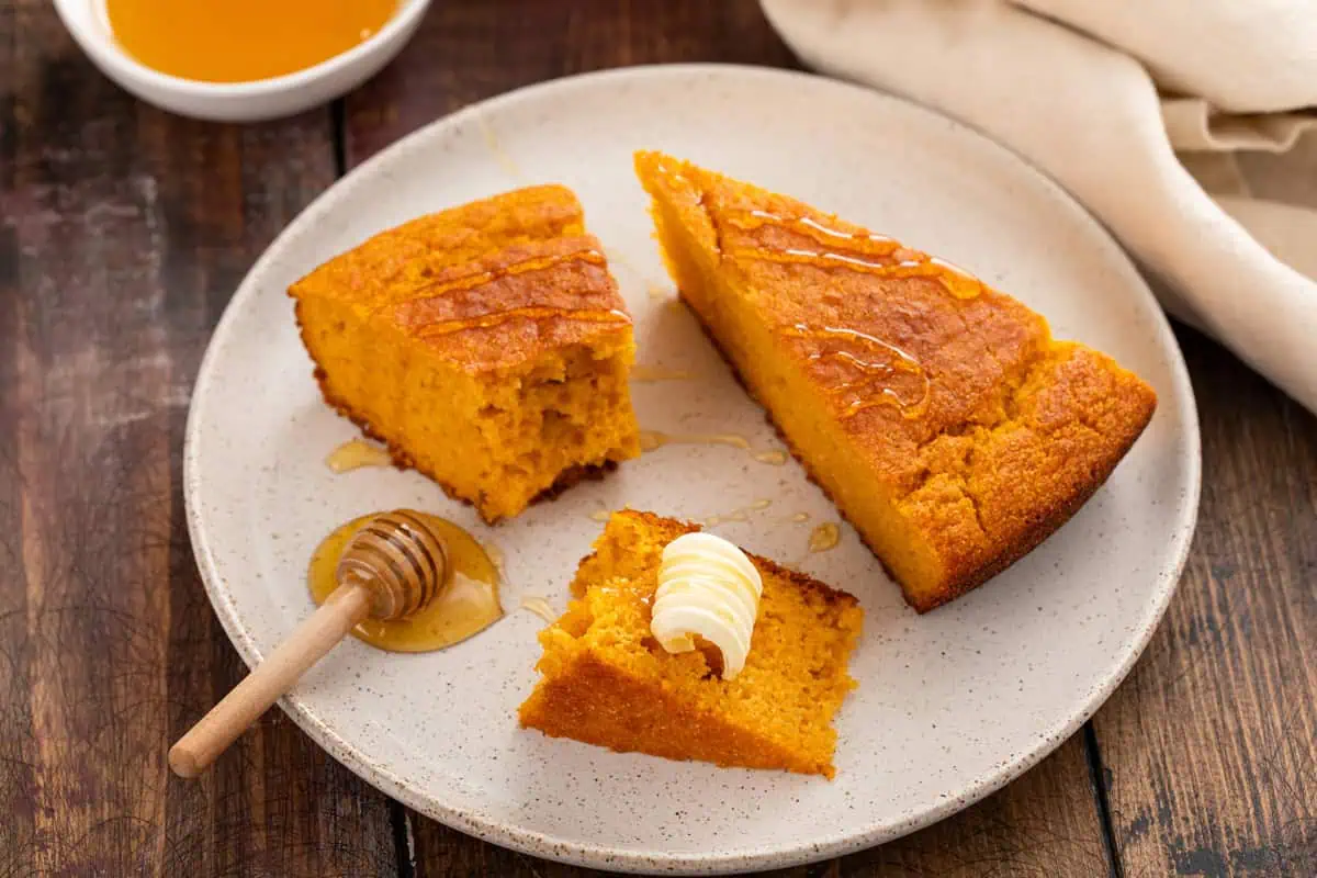 Plated pieces of sweet potato cornbread topped with butter and honey.