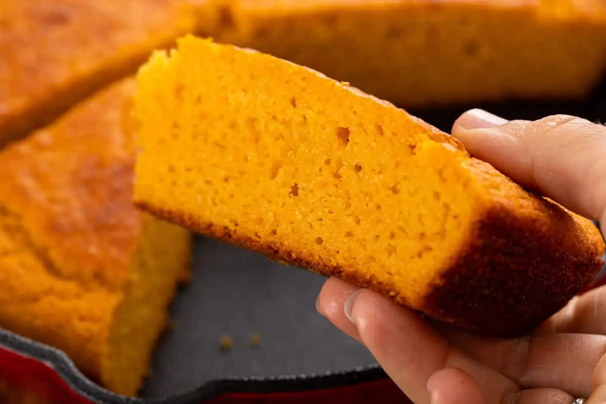 Hand holding a piece of sweet potato cornbread to show the crumb.