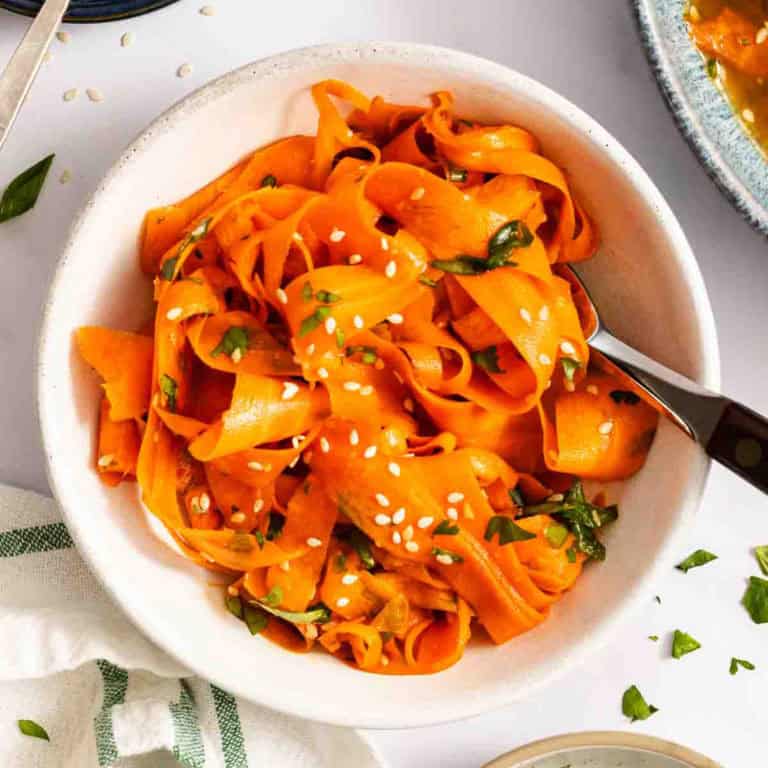Overhead view of a fork in a white bowl of shaved carrot salad.